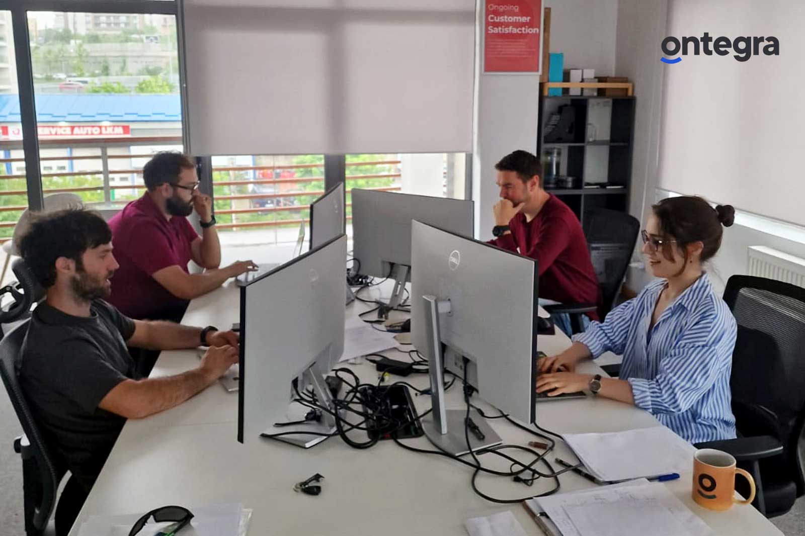 A group of software developers discussing over monitors in a light-filled office, with a focus on teamwork and satisfaction.